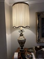Front view of the vintage crystal and brass lamp with fabric shade illuminated, showing the detailed etching on the lamp body, brass base, and hanging crystal accents.