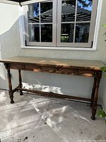 Full view of vintage wooden library table under window on tiled floor. Shows carved legs and wood grain beneath glass top.