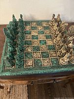 Full view of vintage Mayan/Aztec chess set on the carved board, green and natural stone color pieces arranged.