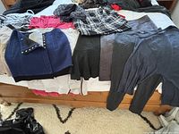 Lot of women's skirts and clothing items arranged on bed showing variety of colors and materials including plaid, navy, black, grey, and knitwear.