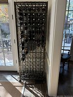 Front view of the tall wrought iron wine rack showing multiple stored bottles and intricate scroll design.