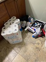 Photo of bathroom floor with stacked packs of toilet tissue and cluster of personal care items including hair dryers, toothbrushes, and packaging.