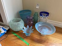 Full lot view showing all items: mosaic glass bowl, blue swirl vase, blue swirl pedestal cake plate, small flower-shaped bowl, purple vase, fish-patterned vase, and daisy flower vase.