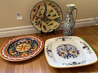 Three decorative plates and one tall vase displayed on wooden floor against a wall, showing the detailed colorful designs and patterns.