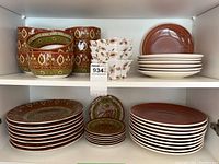 Full view of dish sets on shelves featuring 8 large patterned plates, 7 small patterned plates, 4 patterned bowls, and complementary mauve large and small plates.