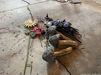 Metal garden decor items and solar lights arranged on concrete floor, showing variety of flower stakes, butterfly stake, metal mushroom stakes, and many solar lights.