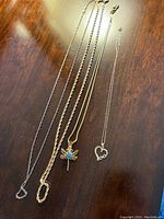 Five necklaces on a wooden surface showing various chain styles and two pendant necklaces including a dragonfly with turquoise and heart pendant.