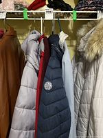 Side view of coats hanging on rack, showing grey, maroon, navy, light beige coats with fur hood