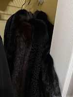 Two black fur coats hanging side by side in closet showing curly and sleek textures