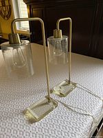 Pair of modern table lamps positioned on a textured white surface showing clear bases, brass stems, and clear glass shades.