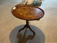 Full view of the oval parlour table standing on a concrete floor, showing the full table including its three-legged base and oval tabletop.