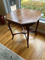 Octagonal wooden side table photographed near a window on hardwood floor, showing overall structure and finish.