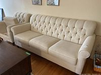 Full view of ivory upholstered 3-seat sofa with tufted back and rolled arms