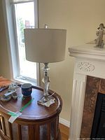 Full view of the modern table lamp showing the white drum shade, glass base with chrome accents, and overall height on a wooden side table.