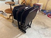 Folded black wooden TV tables nesting on matching stand in basement setting