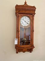 Full view of carved wood pendulum wall clock hanging on wall