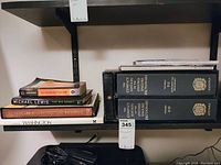 Books including two volumes of The Concise Oxford English Dictionary, several other books stacked including The Big Short and Notable American Houses, and a magnifying glass on a shelf.