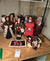 Wide view of Byers' Choice Christmas caroler figures arranged on a wooden surface showing nine figures and a photo of similar carolers.