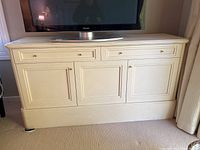 Full front view of the wood cabinet with TV on top, showing two drawers and three doors below each with brass knob.