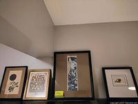 Four framed prints leaning against wall on floor, varied sizes and subjects.