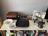 Overview of all items on a table including boxes, plates, bell, small framed art, and dish