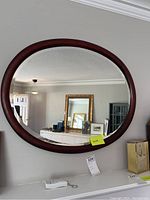 Full front view of oval mirror hanging on wall, showing entire mirror and frame with some reflections visible.