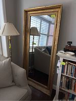 Full view of the vintage wood framed mirror leaning against wall in a living room setting, showing size and style.
