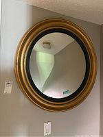 Full view of the round wall mirror showing the gold and black detailed frame, mounted on a wall.