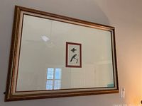 Framed print hung on a wall, showing reflections and surrounding room details.