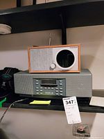 Tivoli Audio One Digital radio stacked on Henry Kloss Model 88 radio on a black shelf with visible remote and hand written note.