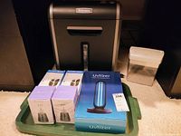 Photo showing lot items on green tray: Fellowes black paper shredder, boxed Uvlizer UV0254 UV disinfection device, two boxed Buzzgone Zap portable heaters, beige Royal paper shredder to side.