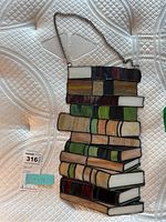 Front view of stained glass panel showing detailed coloring and book shapes, lying flat on a textured white surface.