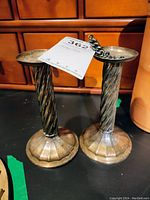 Pair of twisted design sterling silver candle holders with flared bases and a linked sterling silver bracelet with a tag on top of one holder.