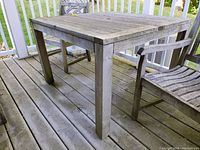 Overall side view of the teak patio table showing legs and weathered tabletop