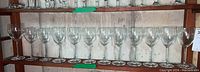 Full row of 14 clear wine glasses with twisted stems arranged side by side on a wooden shelf.