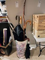 Photo of umbrella stand holding multiple umbrellas and walking sticks, shows curved handles and floral ceramic stand.