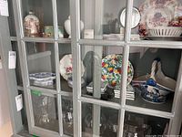A shelf behind a glass cabinet showing varied ceramic plates and bowls including Wedgwood and Delft style pieces.