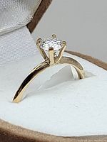 Close-up side view of 10K yellow gold solitaire ring with a round moissanite gemstone set with prongs on the band, mounted in a white ring holder.