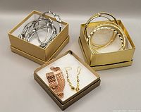 Three boxes displaying the bangles and jewelry included in the lot, showing the gold and silver toned bangles with various textures and patterns, and the bracelet and earrings in a box with white padding.