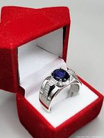 Men's silver ring with large blue sapphire set in a polished band inside a red velvet star-shaped ring box.