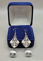Two pairs of silver earrings, one hanging with openwork floral design and one small textured stud pair, displayed in a blue velvet box.