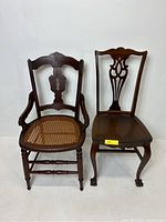 Two carved wooden chairs side by side on a white background, one with cane webbing seat and armrests, the other with solid seat and ball & claw feet.