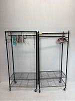 Two black metal garment racks side by side, each with bottom wire shelves and adjustable hanging bars, lockable wheels visible.
