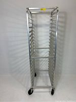 Front view of the aluminum pan rack showing vertical frame and pan slots, mounted on caster wheels.