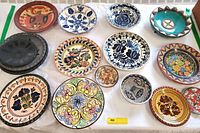 Overview of all thirteen artisan pottery dishes displayed on a white cloth, showing variety in size, color, and design.