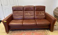 Front view of a three-seat brown leather Mid-Century Modern sofa with visible creasing and wear on cushions and backrests.