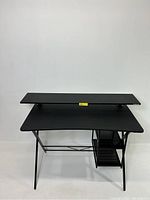 Front view of black metal two-tier computer desk with elevated monitor shelf and main work surface.