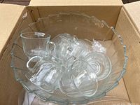 Clear glass punch bowl containing multiple clear glass cups with handles, all inside an original cardboard box.
