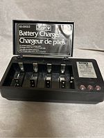Opened Pulser battery charger showing multiple charging slots and a label indicating compatibility with AA, AAA, C, D, and 9V Ni-CAD batteries