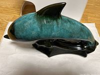 Side view of ceramic dolphin figurine showing blue-green coloration and black ceramic base.